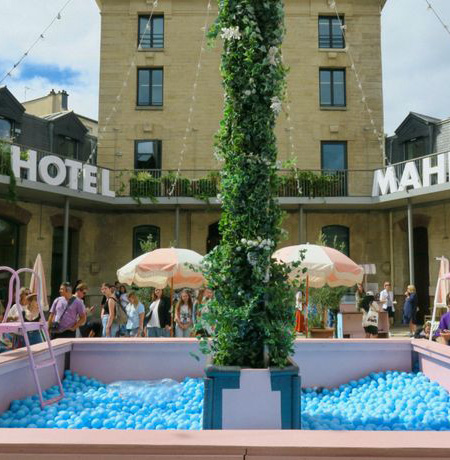 Façade de l’Hôtel Mahfouf avec une fontaine végétale entourée d’une piscine de balles bleues, ambiance estivale.